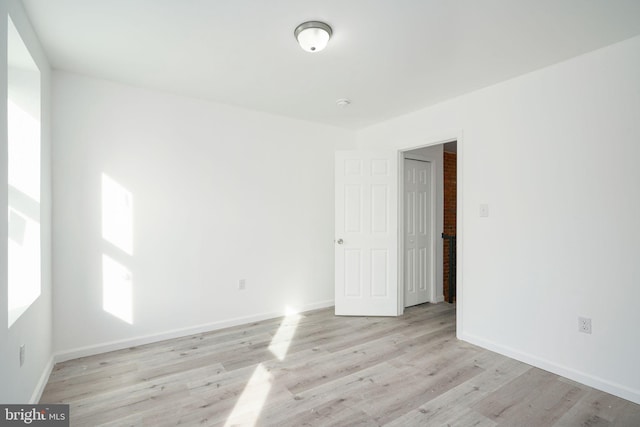 spare room with brick wall and light wood-type flooring