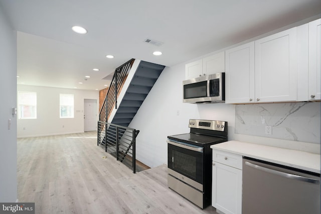 kitchen with white cabinetry, backsplash, light hardwood / wood-style floors, and stainless steel appliances