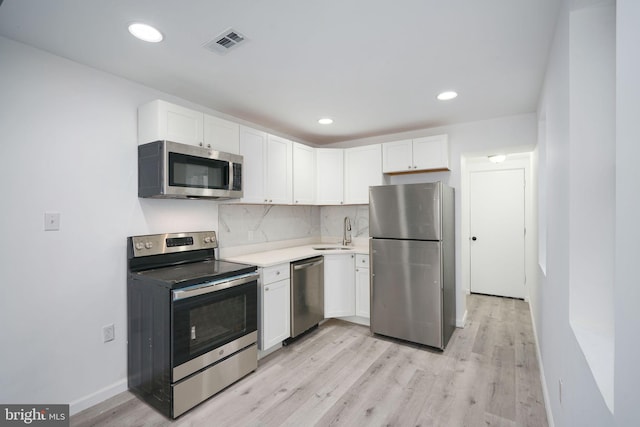 kitchen with backsplash, white cabinetry, appliances with stainless steel finishes, and light wood-type flooring