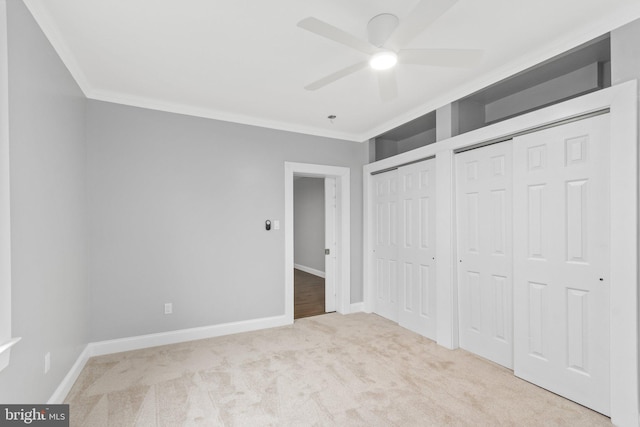 unfurnished bedroom featuring ceiling fan, light colored carpet, ornamental molding, and multiple closets