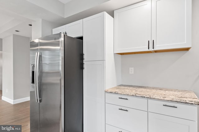 kitchen featuring white cabinets, stainless steel fridge with ice dispenser, hardwood / wood-style flooring, and light stone countertops