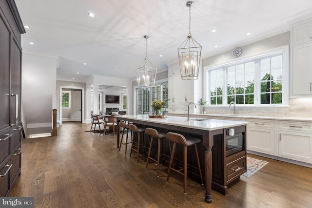 kitchen featuring white cabinets, a center island with sink, dark hardwood / wood-style floors, backsplash, and ornamental molding