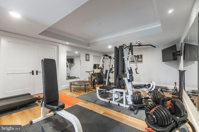 exercise area with light hardwood / wood-style flooring, ornamental molding, and a raised ceiling