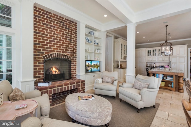 living room with built in shelves, crown molding, ornate columns, and a brick fireplace