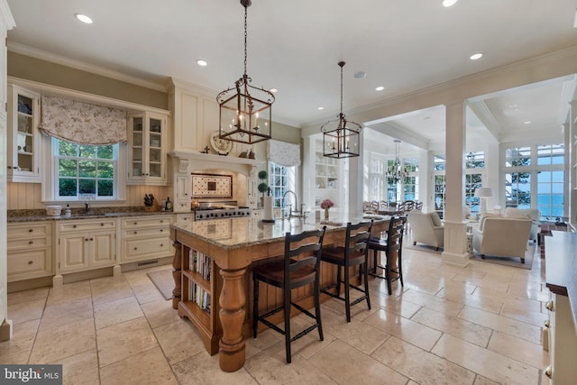 kitchen with light stone countertops, tasteful backsplash, crown molding, cream cabinets, and an island with sink