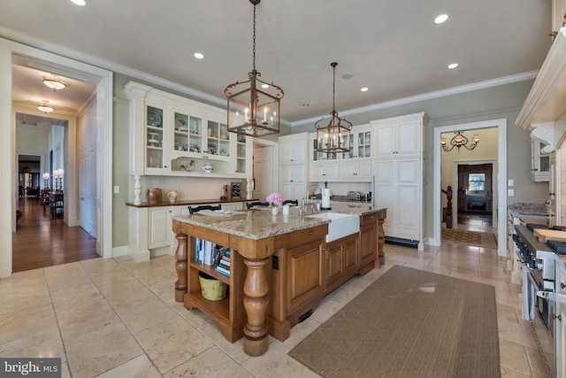 kitchen with light stone countertops, ornamental molding, a kitchen island with sink, sink, and pendant lighting