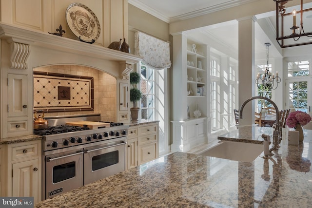 kitchen with sink, light stone counters, crown molding, range with two ovens, and cream cabinetry