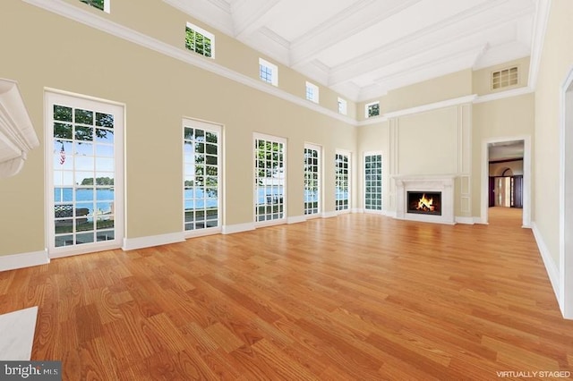 unfurnished living room with crown molding, a towering ceiling, beamed ceiling, and light wood-type flooring