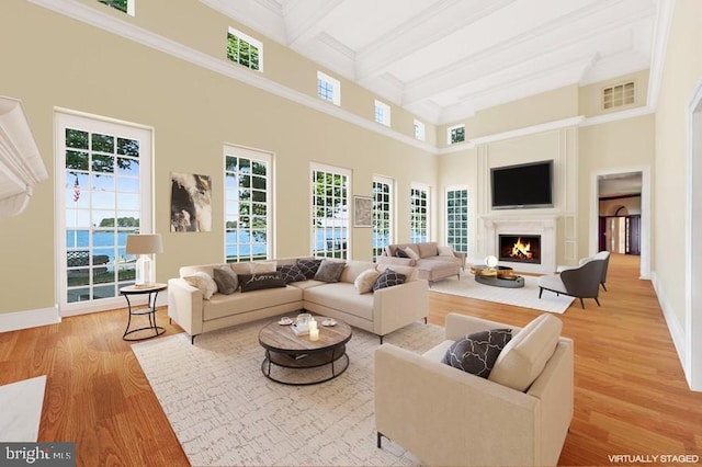 living room with beam ceiling, light wood-type flooring, crown molding, and a towering ceiling