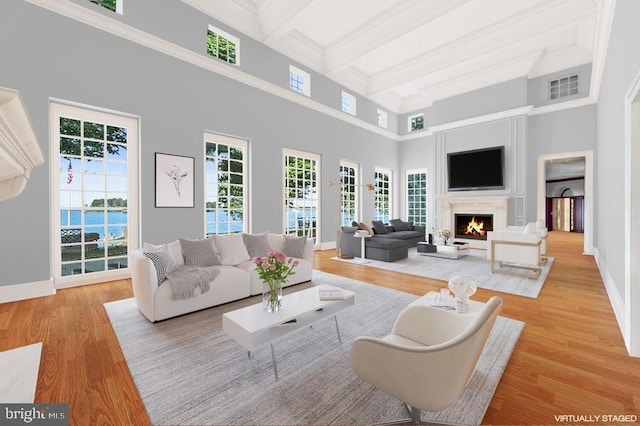 living room with a water view, a towering ceiling, beamed ceiling, and light wood-type flooring