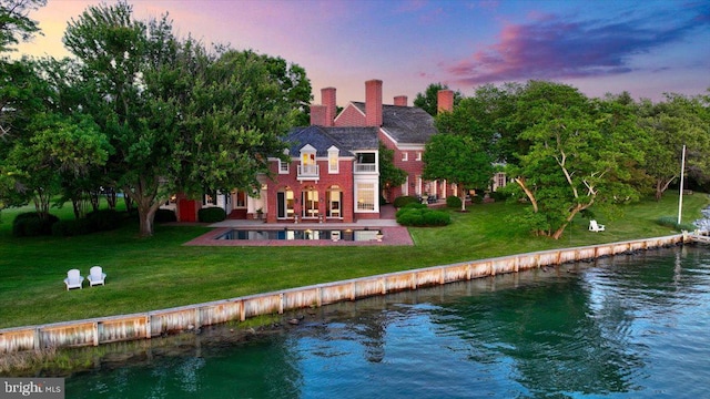 back house at dusk with a yard, a water view, and a patio