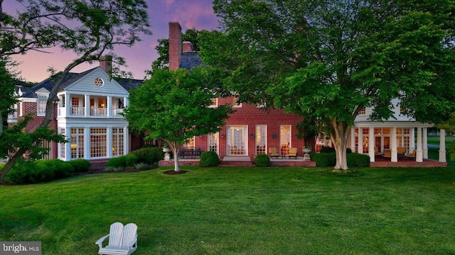 back house at dusk featuring a yard, a balcony, and a patio area