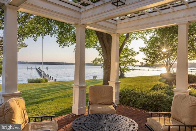 patio terrace at dusk featuring a boat dock, a water view, and a yard