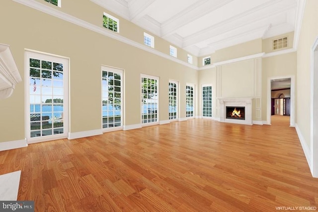 unfurnished living room featuring a towering ceiling, light hardwood / wood-style flooring, beamed ceiling, and ornamental molding