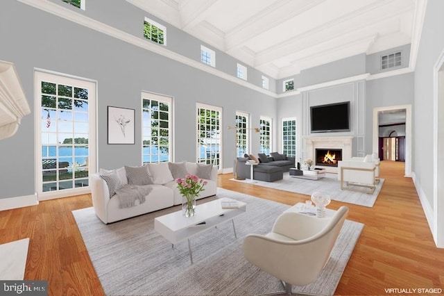 living room with beam ceiling, light hardwood / wood-style floors, a water view, and a high ceiling