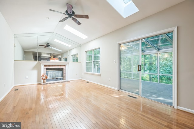 unfurnished living room with wood-type flooring, ceiling fan, a brick fireplace, and lofted ceiling with skylight