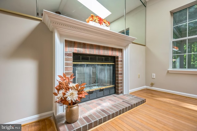 interior details featuring wood-type flooring, a brick fireplace, and a skylight