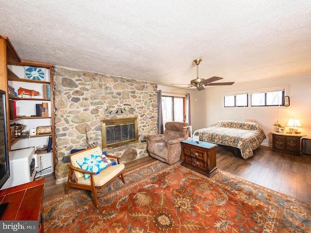 bedroom featuring ceiling fan, a fireplace, dark wood-type flooring, and a textured ceiling