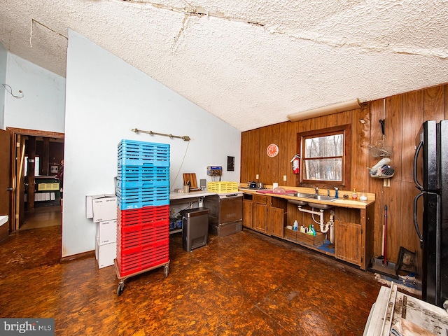 kitchen featuring black refrigerator, a textured ceiling, vaulted ceiling, and wood walls