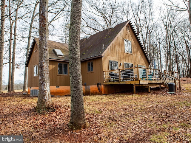 rear view of property featuring crawl space, a shingled roof, central AC unit, and a deck