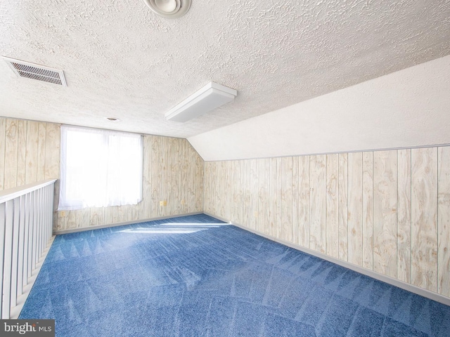 additional living space with lofted ceiling, a textured ceiling, wood walls, visible vents, and carpet