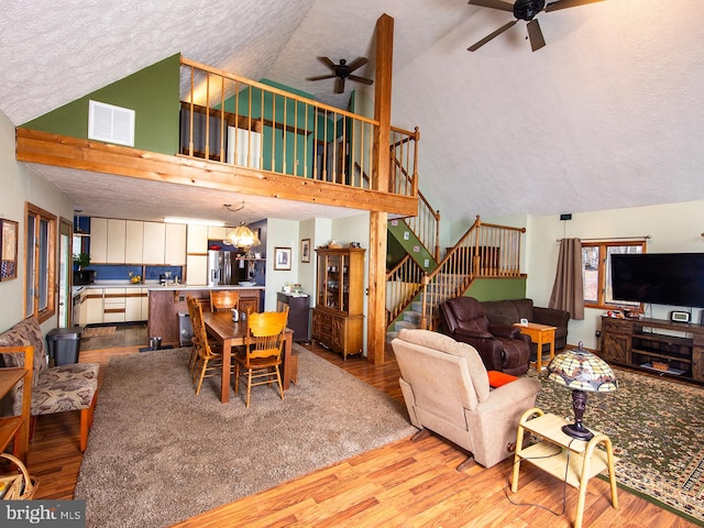 living area featuring light wood-style floors, visible vents, stairway, and ceiling fan with notable chandelier