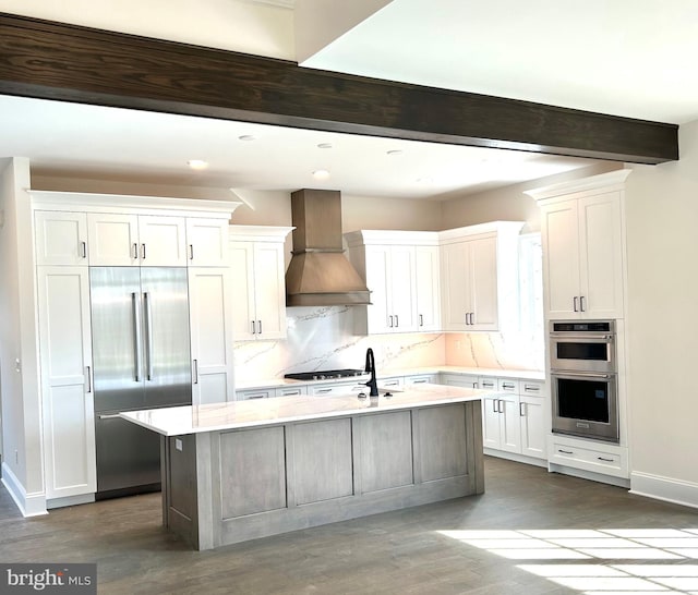 kitchen featuring premium range hood, stainless steel appliances, white cabinetry, a kitchen island with sink, and dark hardwood / wood-style flooring