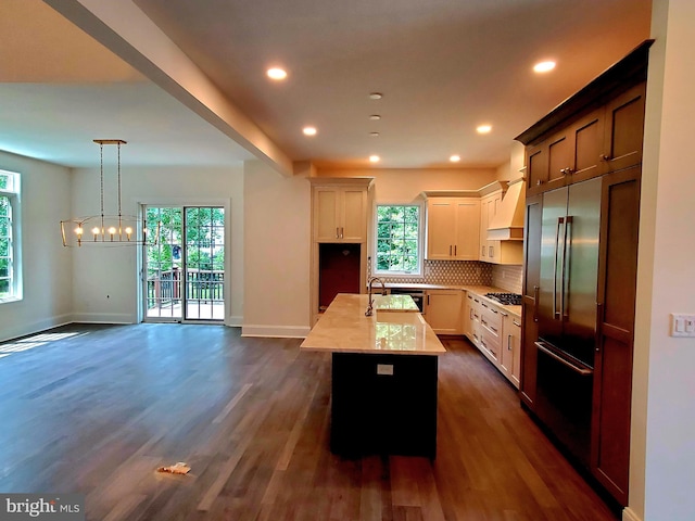 kitchen featuring decorative light fixtures, dark wood-type flooring, a wealth of natural light, and a kitchen island with sink