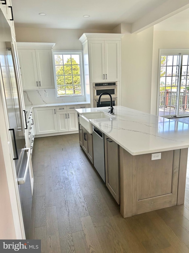 kitchen featuring appliances with stainless steel finishes, white cabinetry, light stone counters, a kitchen island with sink, and dark hardwood / wood-style flooring