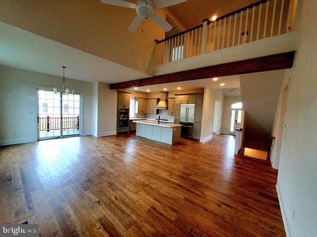 unfurnished living room featuring sink, ceiling fan with notable chandelier, a high ceiling, and wood-type flooring