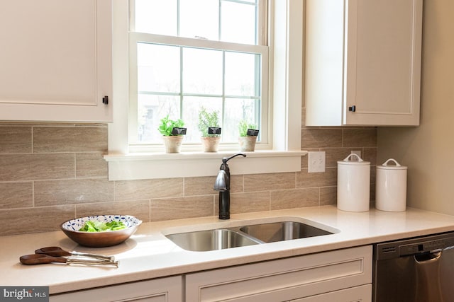 kitchen featuring white cabinetry, backsplash, dishwashing machine, sink, and a wealth of natural light