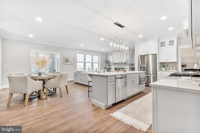 kitchen with a breakfast bar, appliances with stainless steel finishes, white cabinets, a center island with sink, and light hardwood / wood-style flooring