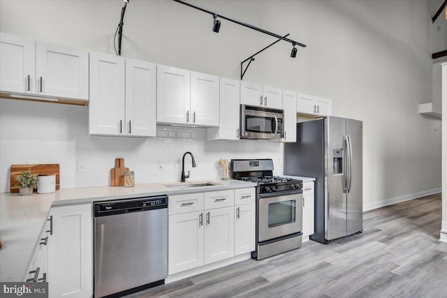 kitchen with appliances with stainless steel finishes, white cabinetry, light hardwood / wood-style floors, and track lighting