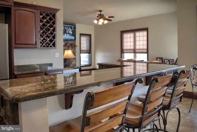 bar with dark stone countertops, ceiling fan, and light tile flooring