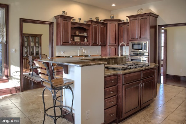 kitchen featuring dark stone countertops, a breakfast bar area, stainless steel appliances, and light tile flooring