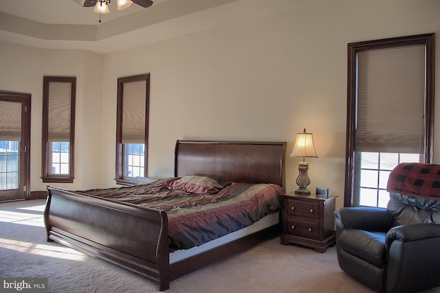 bedroom with light colored carpet, ceiling fan, and a tray ceiling