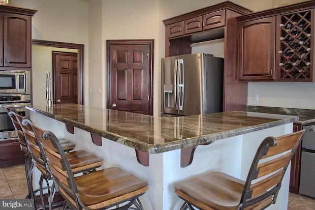 kitchen with appliances with stainless steel finishes, light tile floors, and a kitchen bar