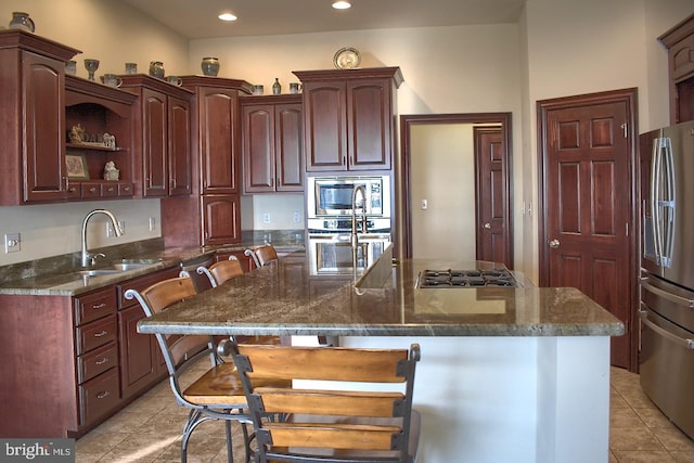 kitchen featuring a breakfast bar area, stainless steel appliances, dark stone counters, a kitchen island with sink, and light tile floors