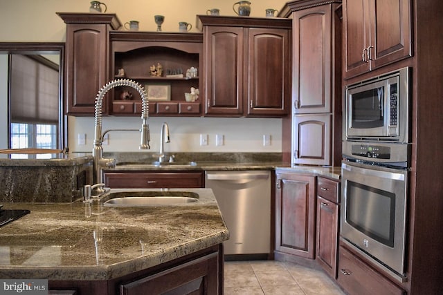 kitchen featuring dark stone countertops, dark brown cabinetry, stainless steel appliances, and light tile floors