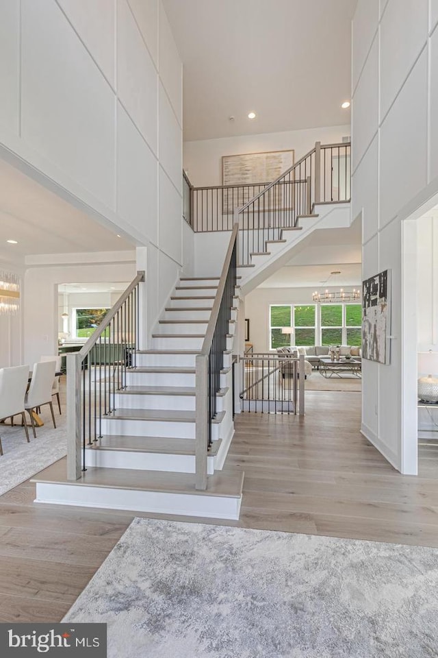 stairway featuring a chandelier, a towering ceiling, and light wood-type flooring