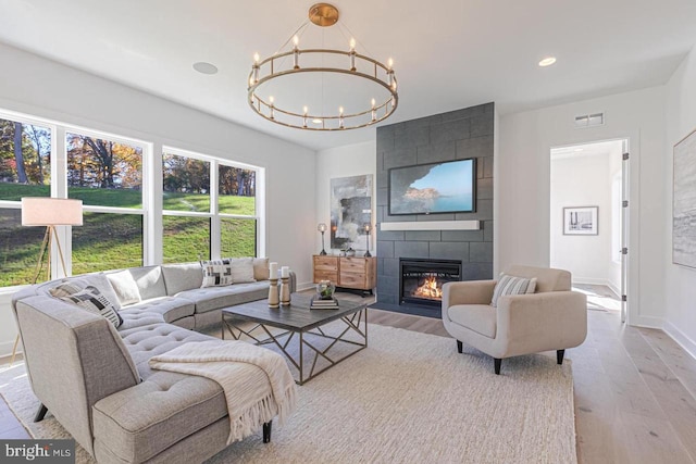 living room with light hardwood / wood-style flooring, a tiled fireplace, and an inviting chandelier