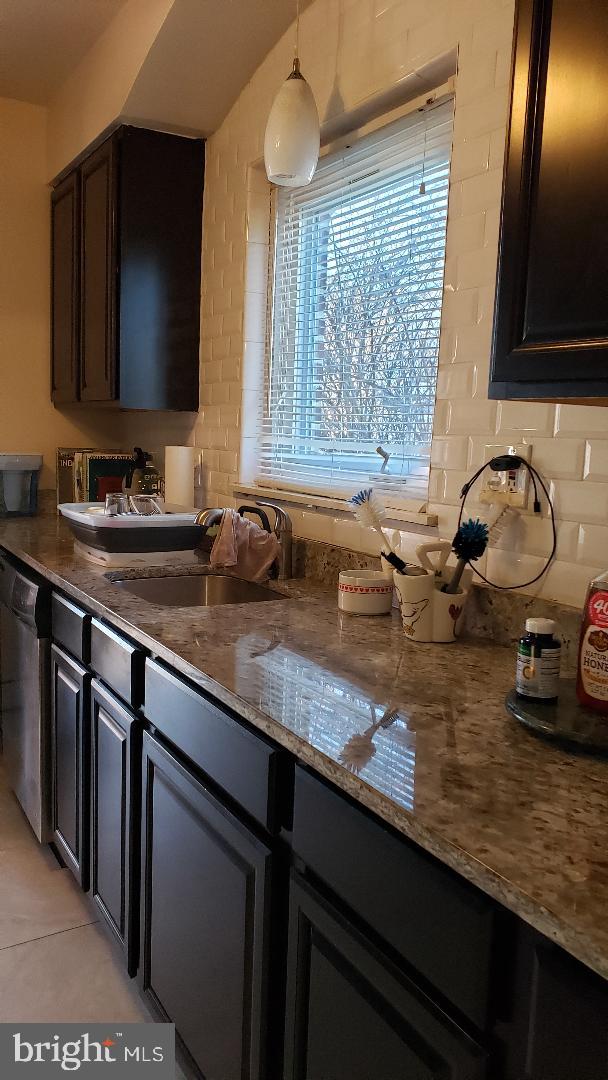 kitchen with dishwasher, sink, hanging light fixtures, dark stone counters, and light tile patterned flooring