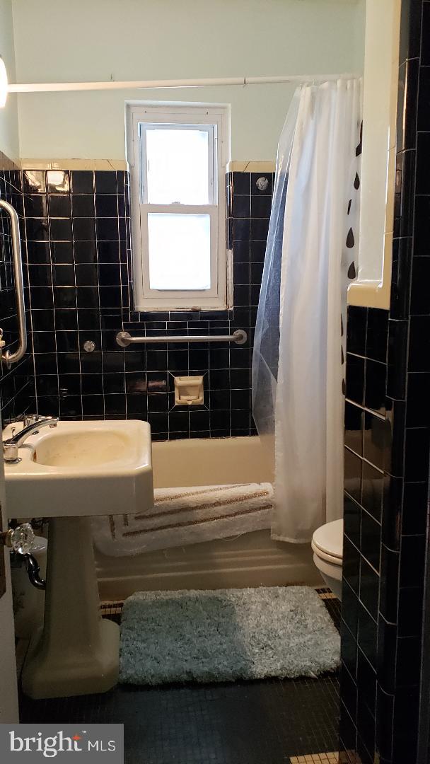 bathroom with toilet, shower / bathtub combination with curtain, and tile walls