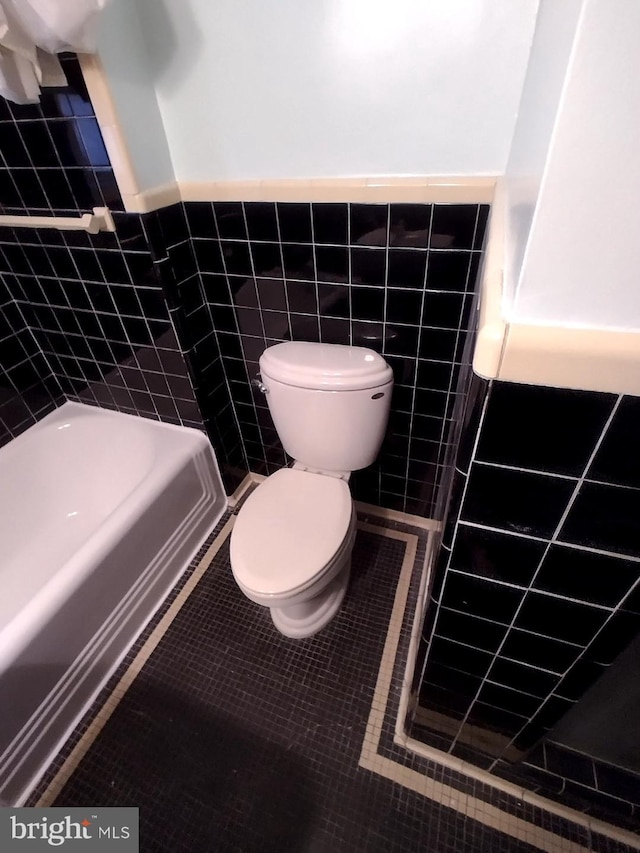 bathroom featuring a washtub, tile patterned flooring, tile walls, and toilet