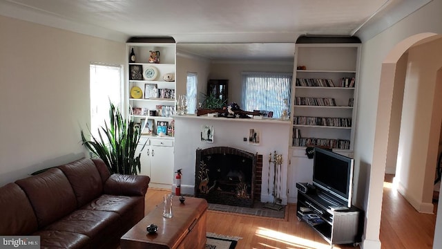 living room with a wealth of natural light, light hardwood / wood-style flooring, crown molding, and a brick fireplace