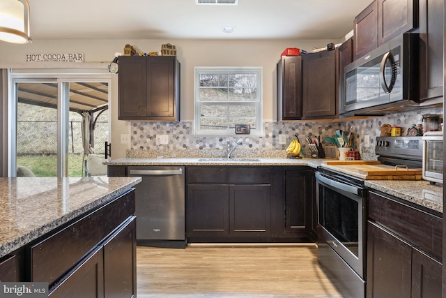 kitchen with dark brown cabinets, light hardwood / wood-style flooring, appliances with stainless steel finishes, backsplash, and sink