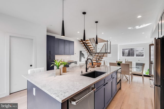 kitchen featuring appliances with stainless steel finishes, light hardwood / wood-style floors, sink, a center island with sink, and light stone counters