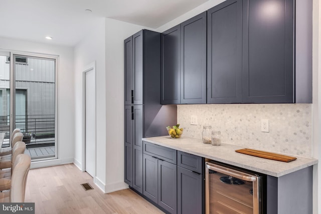 bar featuring light wood-type flooring, backsplash, and beverage cooler