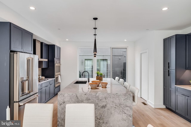 kitchen with light stone countertops, decorative light fixtures, light hardwood / wood-style floors, sink, and stainless steel appliances