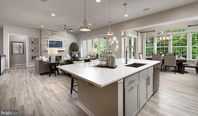 kitchen featuring a center island with sink, light wood finished floors, light countertops, gray cabinetry, and a sink